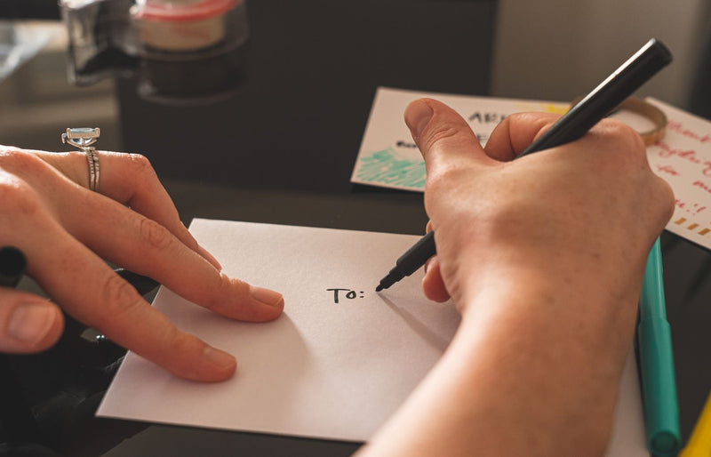 Hands writing on an envelope with marker, emphasizing handwritten correspondence.
