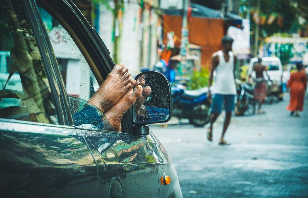Feet resting out a car window in a bustling Indian street, capturing everyday life.