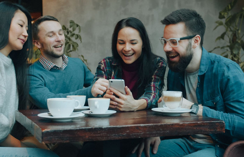 A group of diverse friends laughing and enjoying coffee together indoors.
