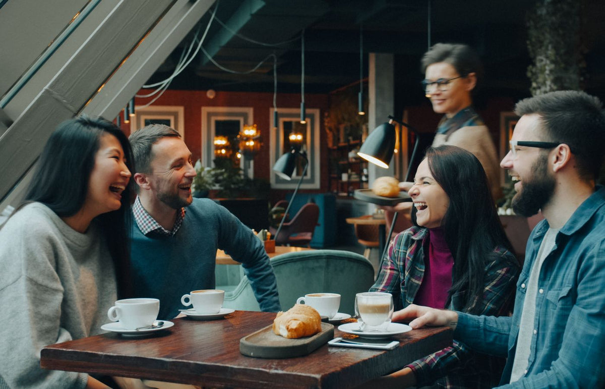 A group of friends laughing and enjoying coffee at a cozy indoor cafe setting.