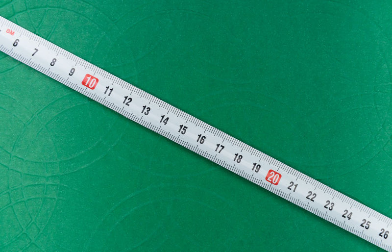 A close-up shot of a tape measure on a textured green background, showing precise measurements.