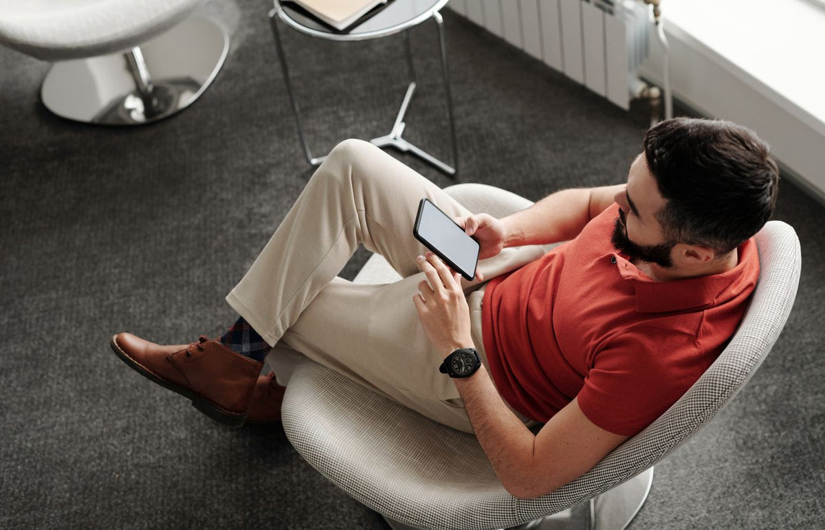 Bearded man in a red polo shirt sitting comfortably, using a smartphone indoors.
