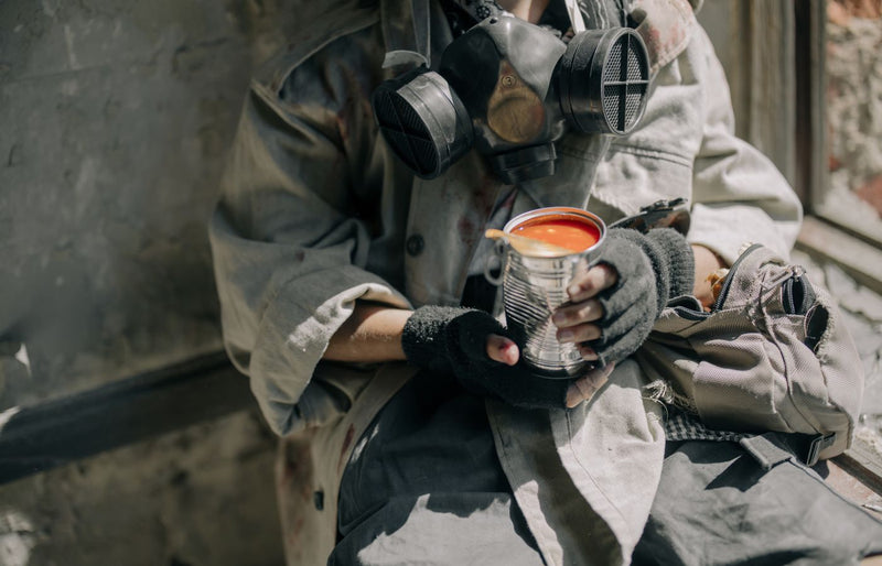 A person wearing a gas mask holding canned tomato soup, symbolizing survival.