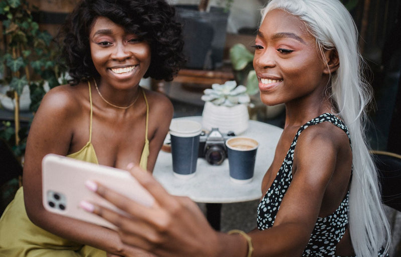 Two smiling women enjoying coffee and taking a selfie together in an outdoor cafe setting.