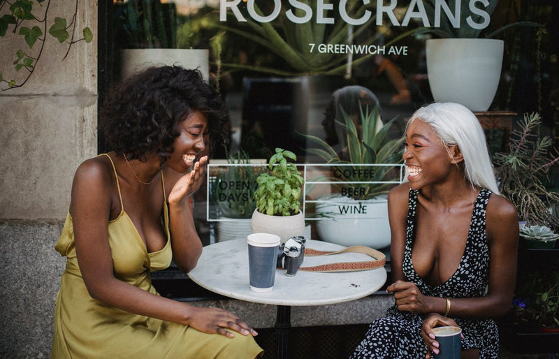 Two friends share laughter over coffee at a café, creating a joyful outdoor scene.