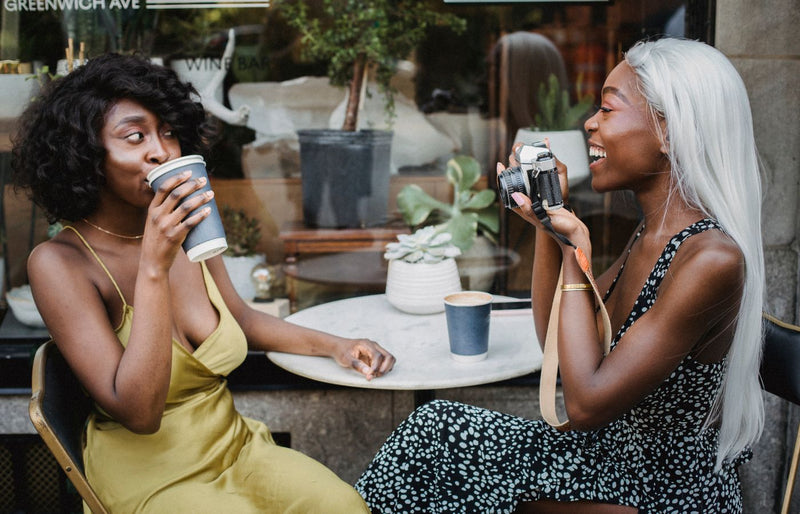 Two women enjoying coffee and photography at a cafe. Relaxed atmosphere and friendship captured outdoors.