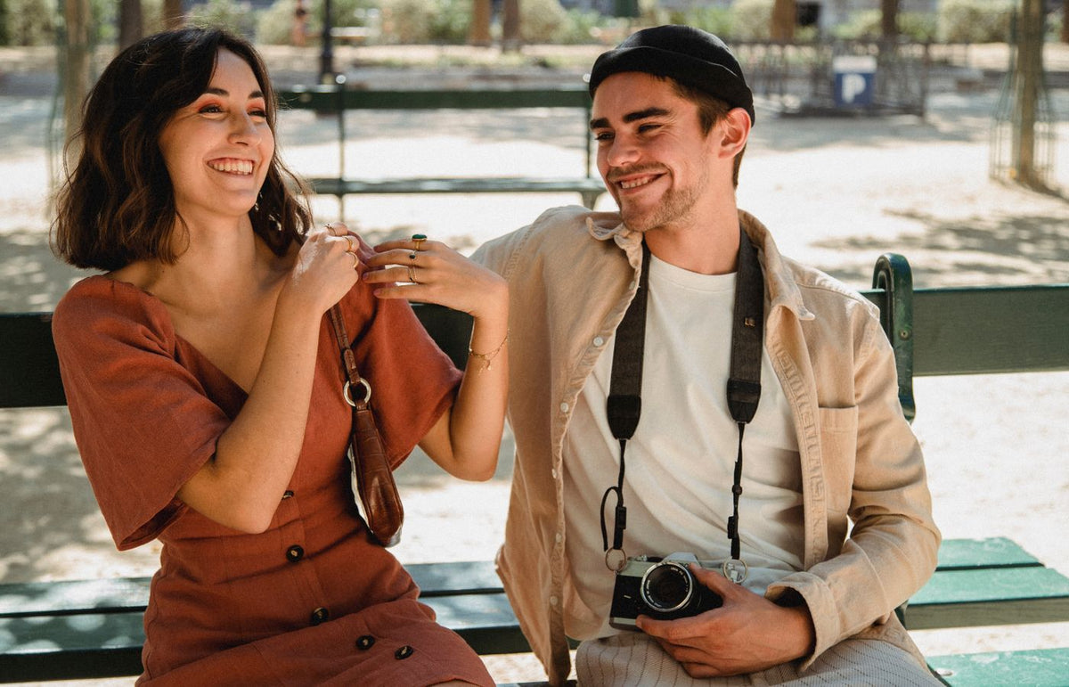 Smiling couple sitting on a bench, enjoying a sunny day outdoors.