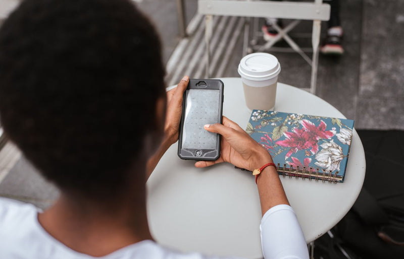 Back view of a woman using a smartphone in a café with a coffee and notebook.