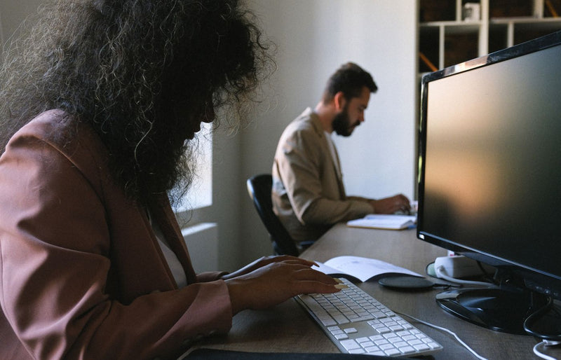 Two professionals concentrating on work in a modern office setting, using computers and notebooks.