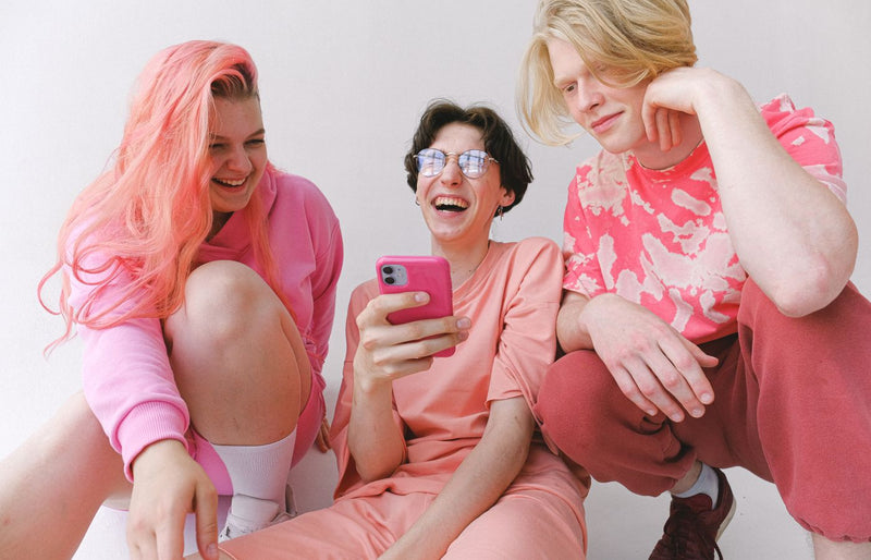 Three friends laughing and enjoying each other's company while looking at a smartphone indoors.