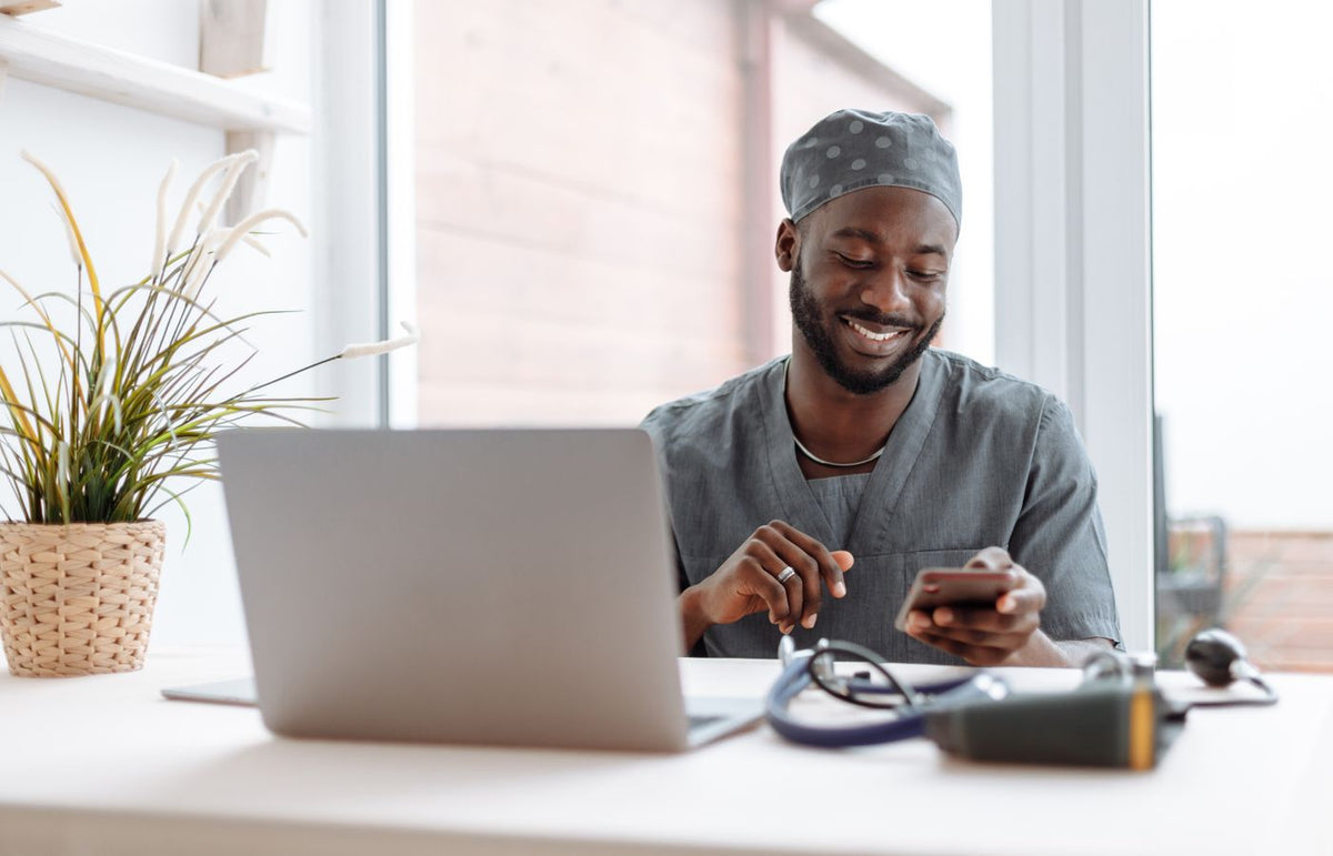 Smiling healthcare professional using phone in office with laptop and medical tools.