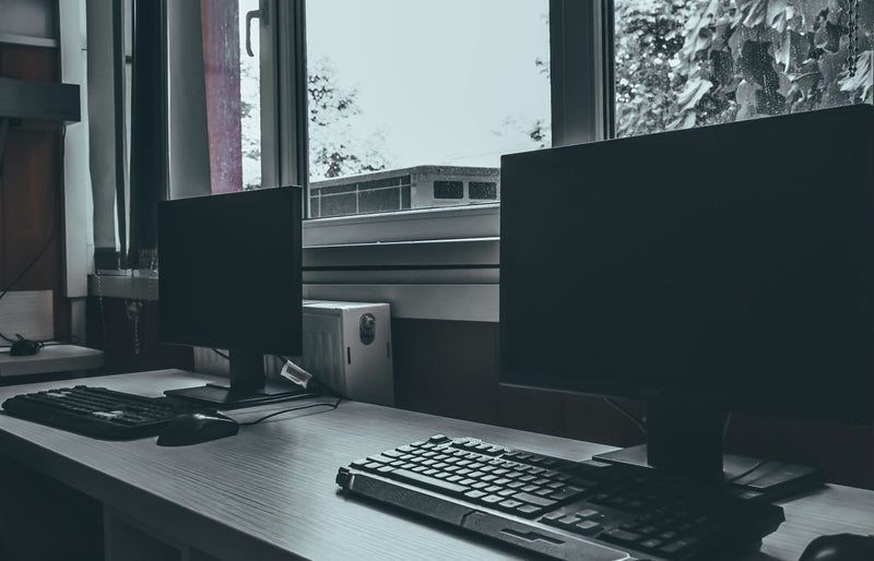 Empty office workspace with two computer monitors by a window, conveying a modern and professional environment.