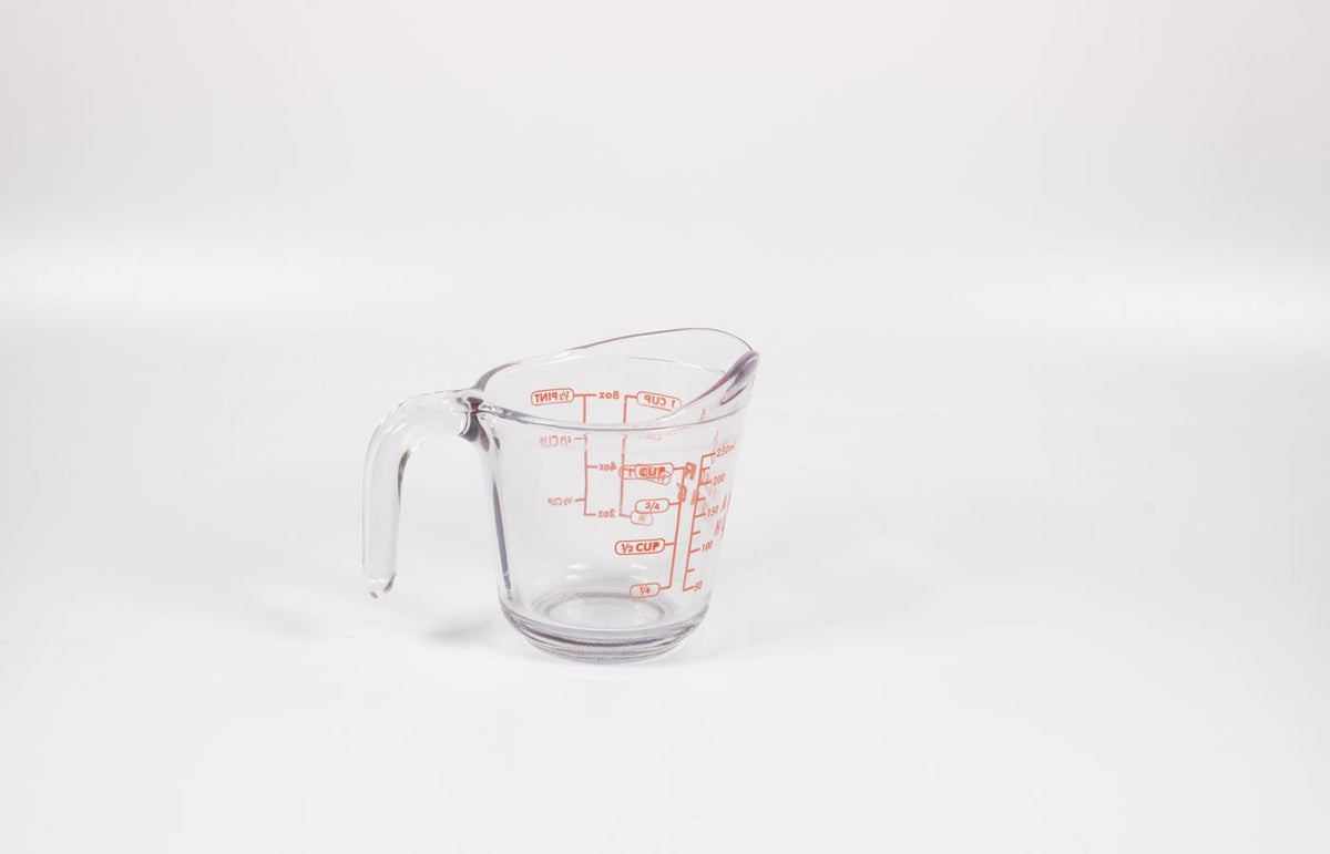 A clear glass measuring cup with red markings on a white background, perfect for culinary use.