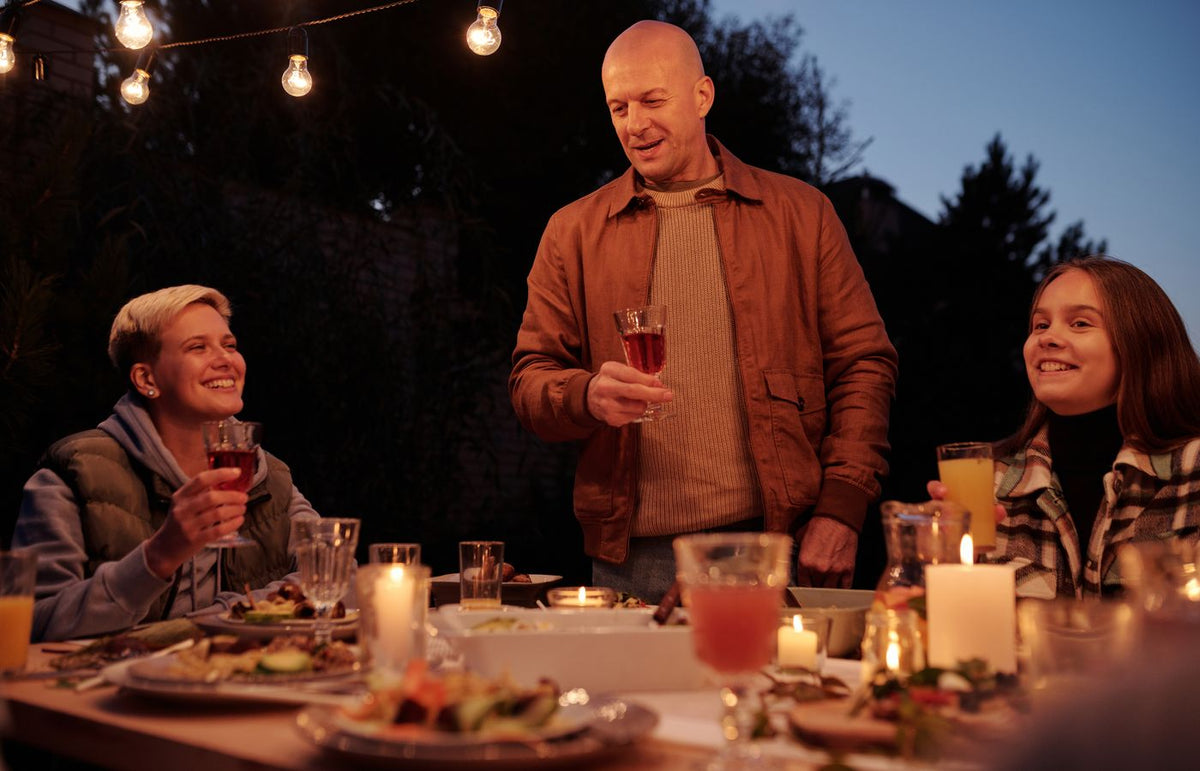 Cozy outdoor family dinner at night with drinks, laughter, and warm lighting.
