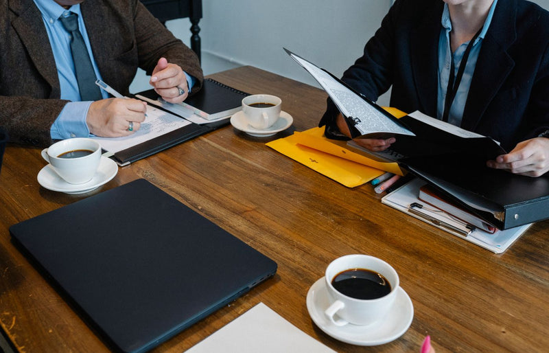 Professional setting with colleagues discussing strategy over coffee at an indoor office.