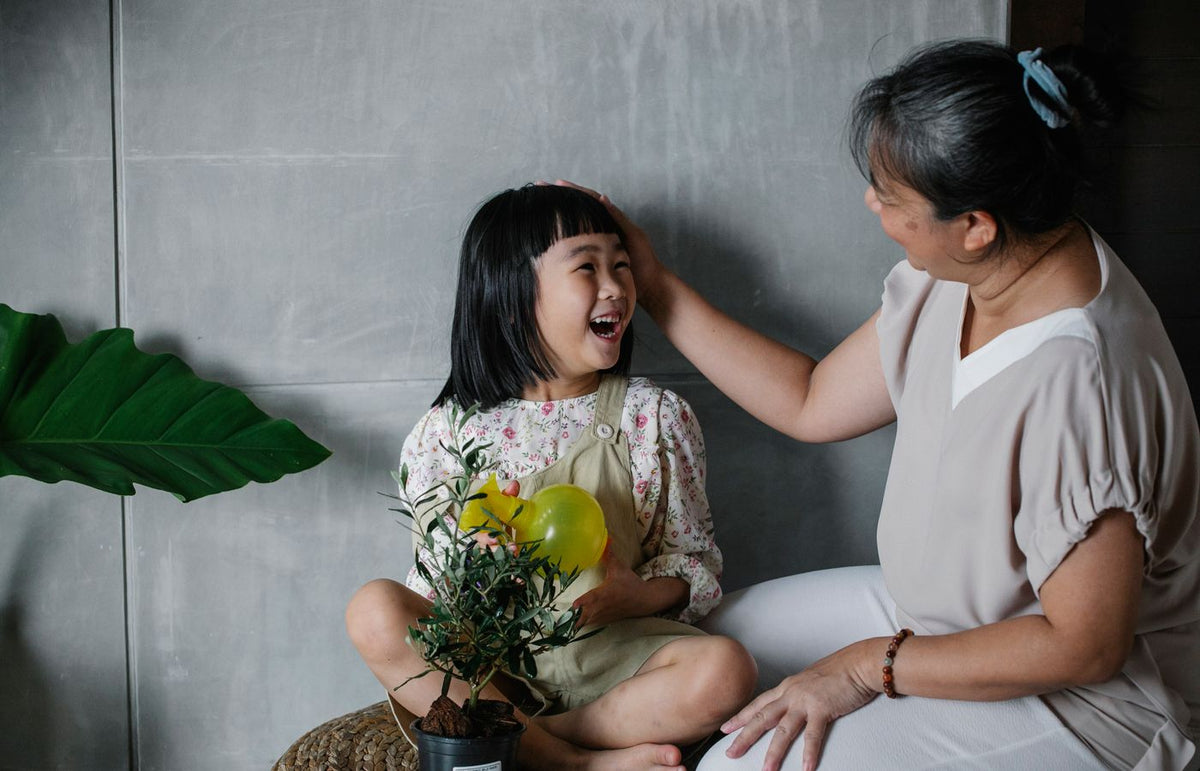 Grandmother and granddaughter laughing and bonding indoors with a potted plant.