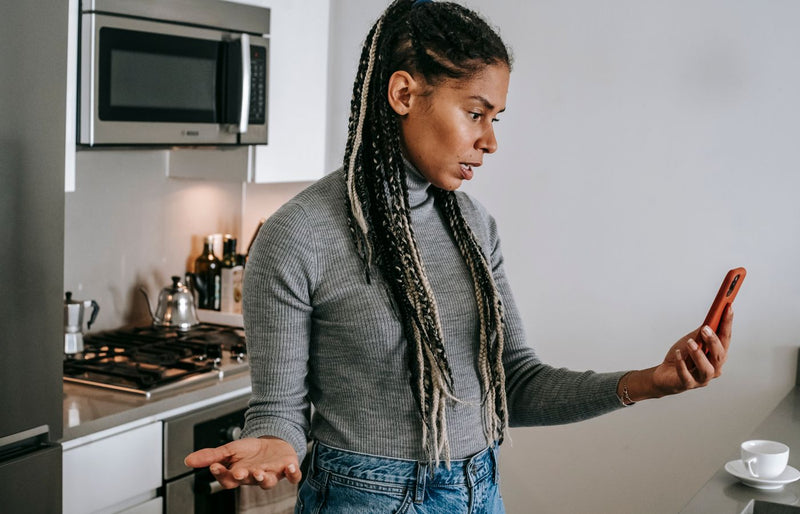 A young woman gesticulates while having a frustrating phone call in a modern kitchen setting.