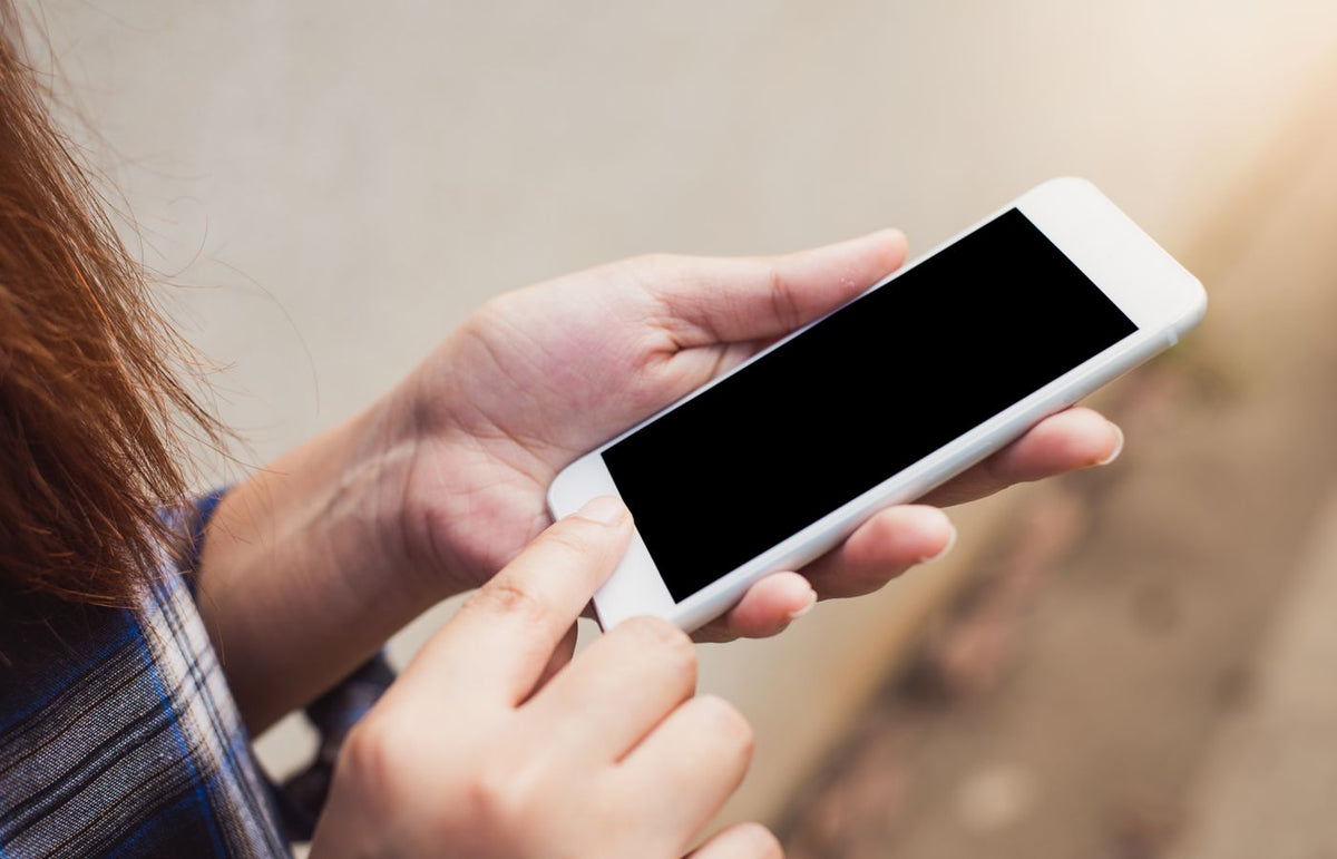 Person holding and using a smartphone outdoors, focusing on hands and screen.