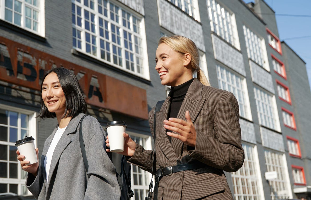 Two women enjoying a sunny day, walking and drinking coffee on a city street.