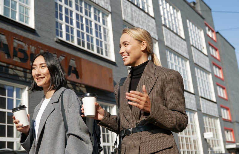 Two women enjoying a sunny day, walking and drinking coffee on a city street.