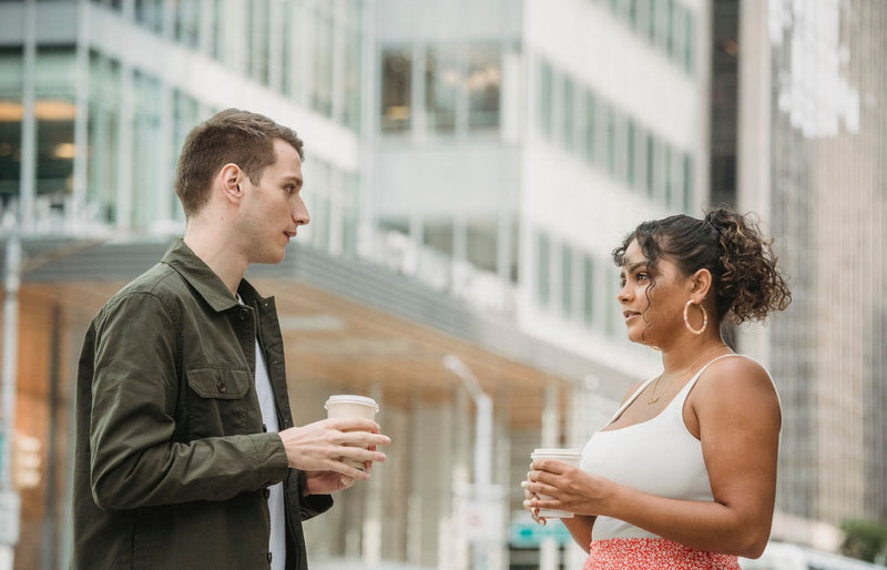 Two young adults enjoying a coffee break outdoors, engaging in conversation amidst an urban setting.