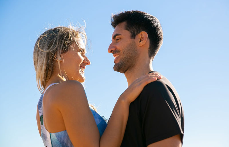 A joyful couple smiling at each other beneath a clear blue sky, symbolizing love and happiness.