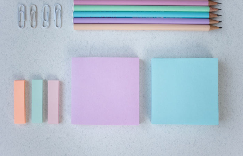 A flat lay of colorful pastel stationery including paper clips, pencils, and sticky notes.
