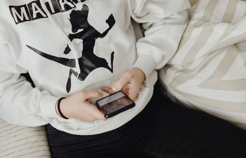 Close-up of a person using a smartphone in a casual hoodie while seated indoors.