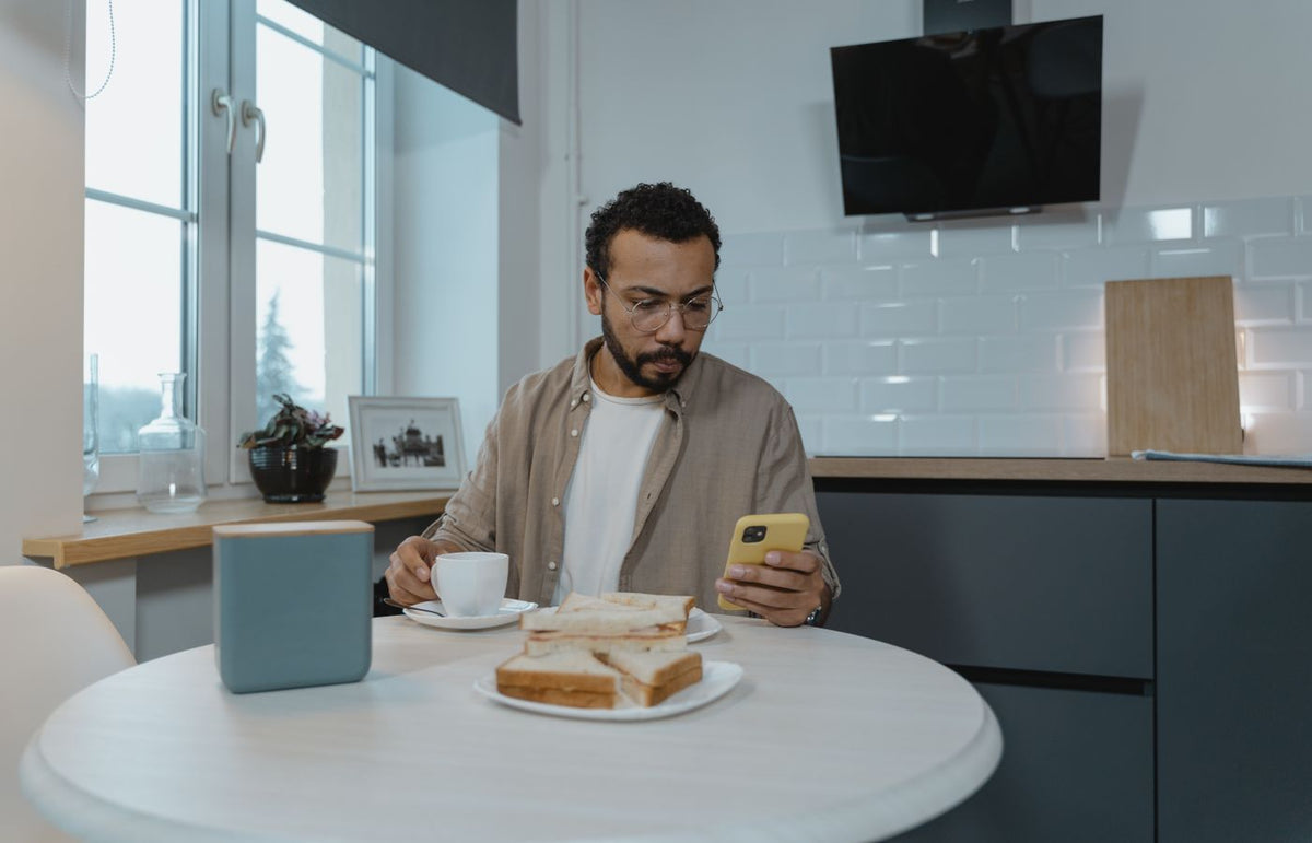 Man sitting at a table with a smartphone and coffee, enjoying breakfast indoors.