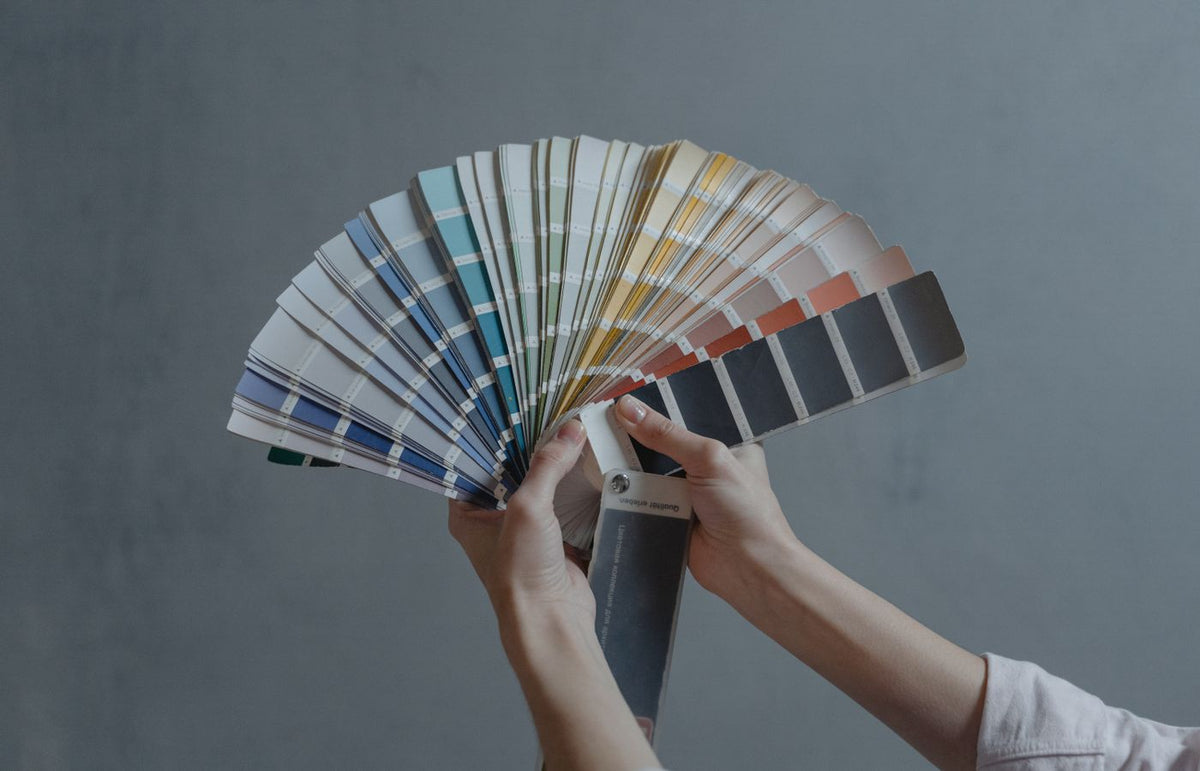 Hands holding a colorful fan of swatches on a gray backdrop, ideal for design themes.