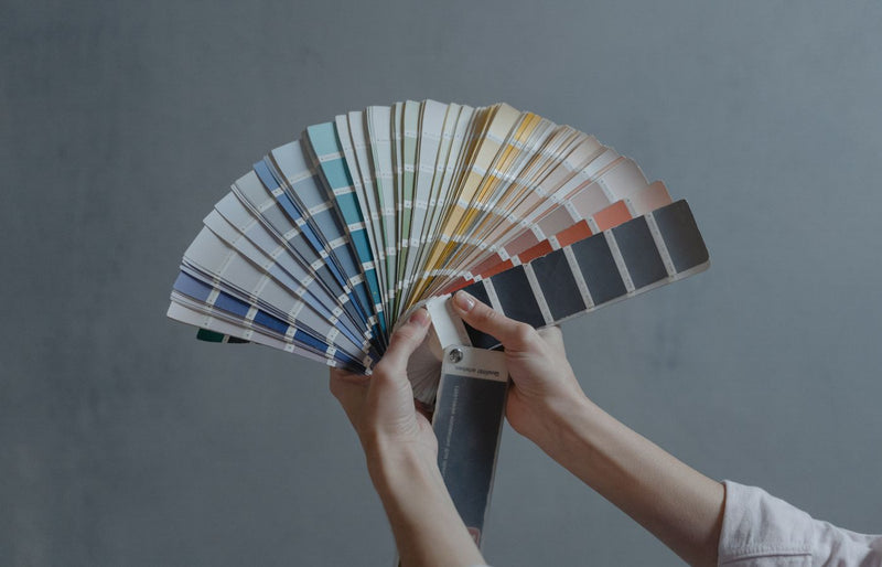 Hands holding a colorful fan of swatches on a gray backdrop, ideal for design themes.