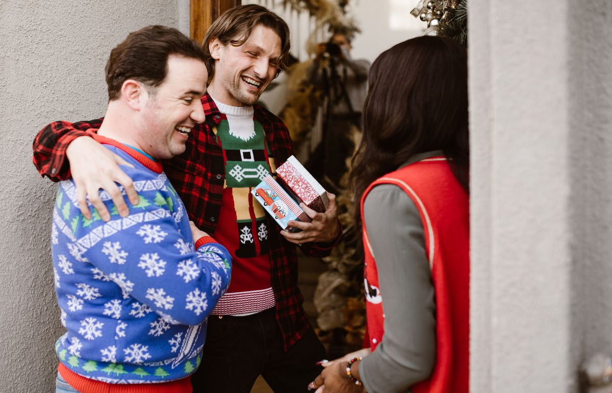 A joyful group of friends wearing Christmas sweaters and exchanging gifts at a holiday gathering.