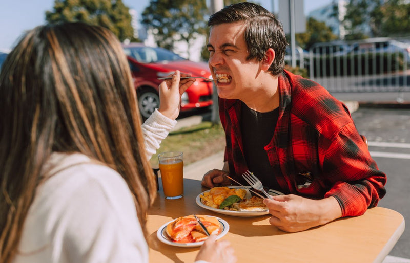 A cheerful couple playfully feeding each other lunch at an outdoor cafe.