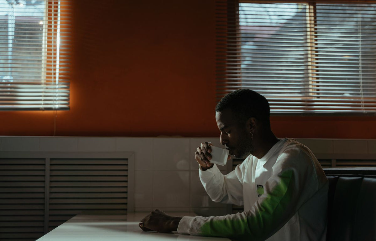 A man seated in a café, enjoying a cup of coffee with sunlight streaming through the windows.