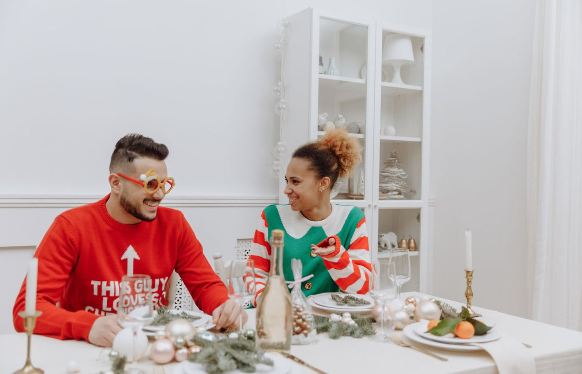 Couple enjoying holiday meal in festive sweaters, embracing Christmas spirit indoors.