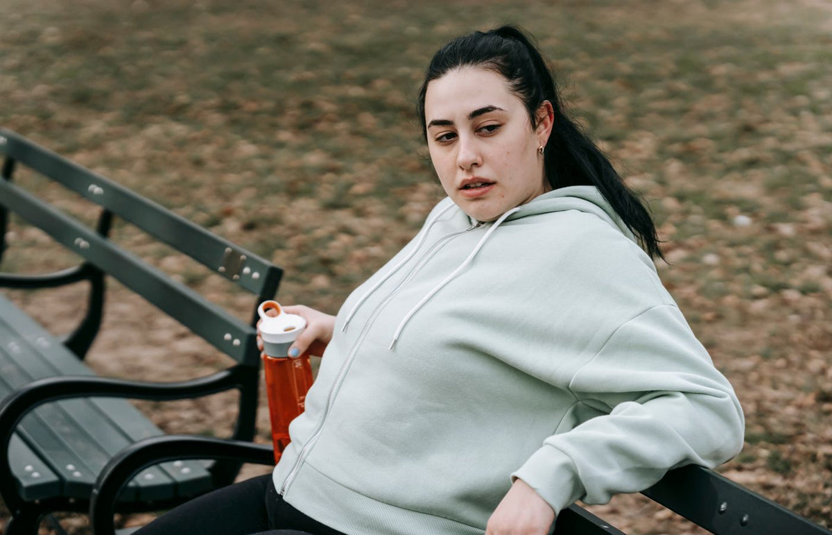 A young woman takes a break on a park bench with a water bottle after exercising outdoors.