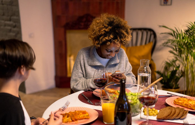 Two friends enjoy a cozy dinner indoors, sharing laughter and conversation over pasta and wine.