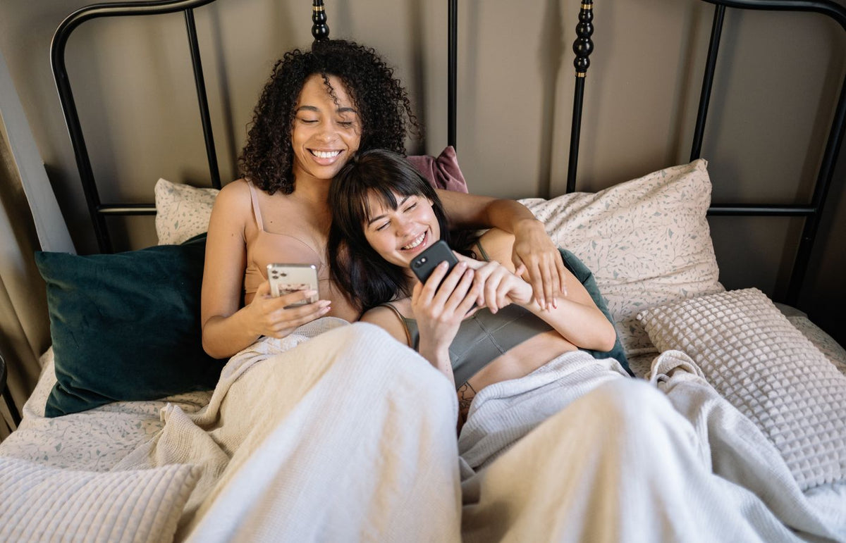 A joyful couple lying in bed using smartphones, sharing sweet moments.