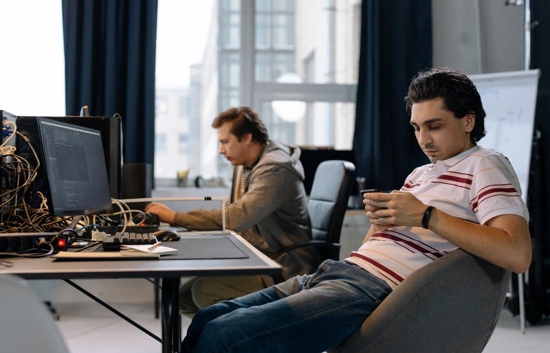 Two men working in a modern office, one on a computer and the other on a smartphone.
