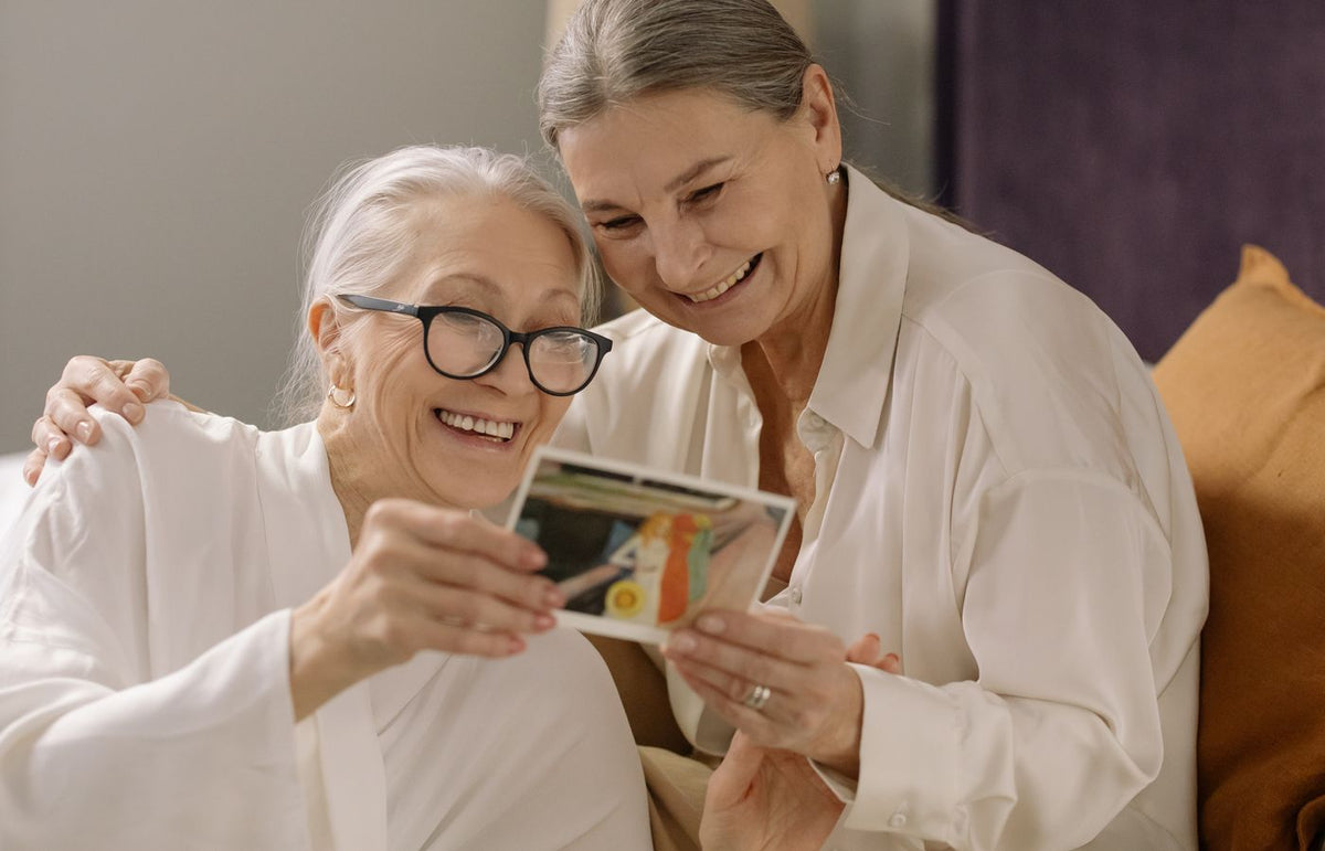 Two elderly women smiling and enjoying old photos, capturing heartfelt memories indoors.