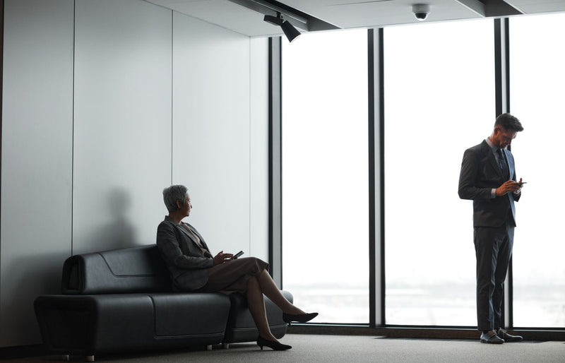 Business professionals in formal attire waiting in a modern office lobby.