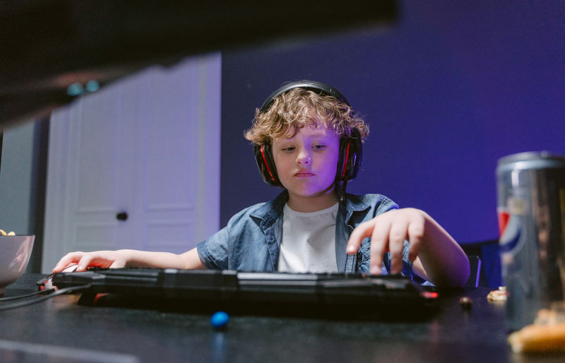 Young boy engrossed in gaming, wearing headphones, in a dimly lit room. E-sports vibe.