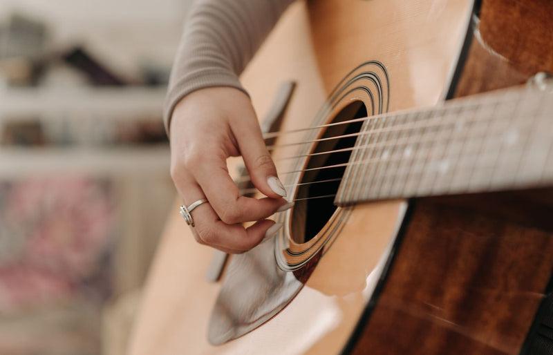 A detailed close-up of a hand playing an acoustic guitar, focusing on the strings and soundhole.