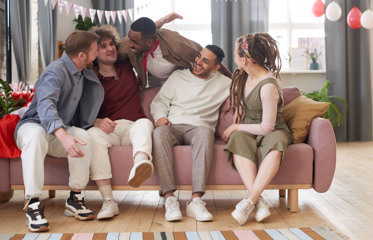 Five diverse friends laughing and bonding on a couch in a cozy indoor setting.