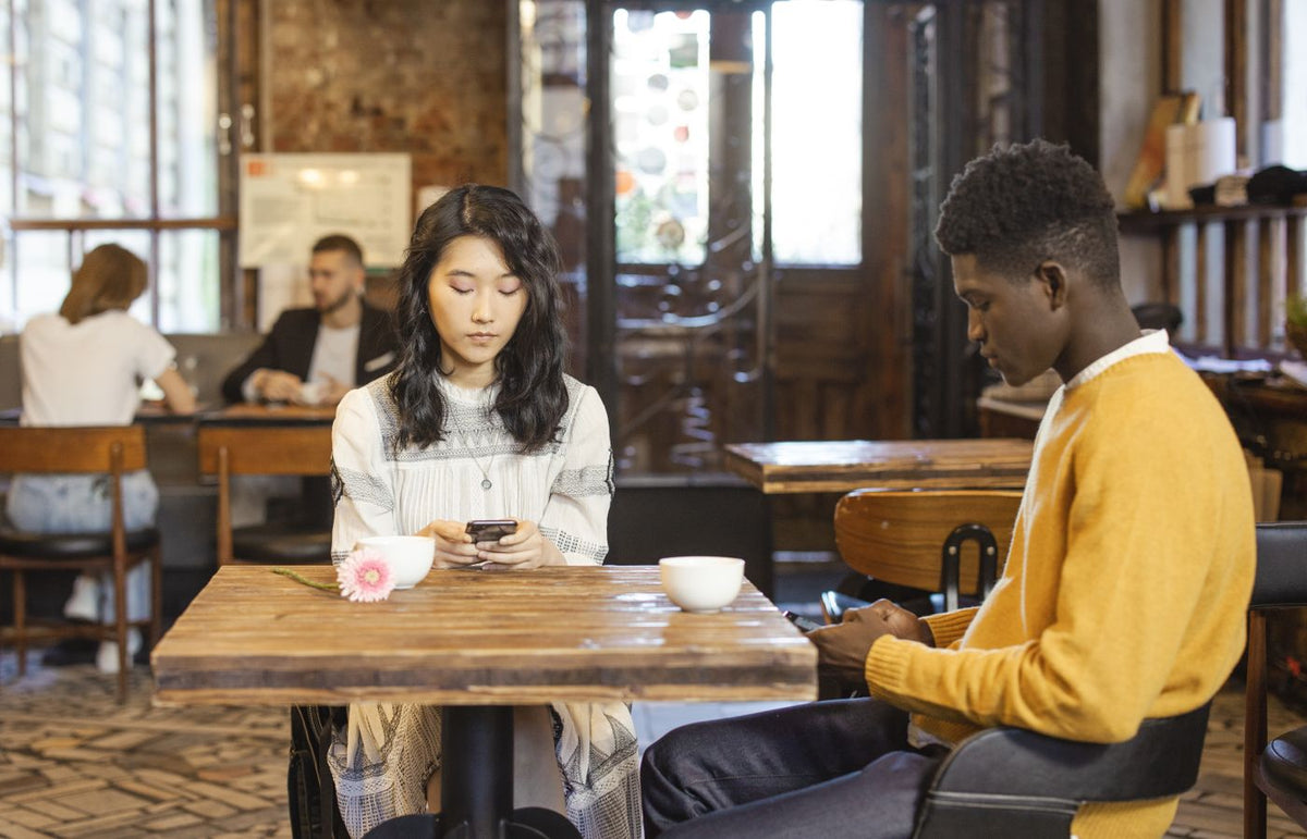 Interracial couple texting while sitting in a modern urban cafe, enjoying a casual meeting.