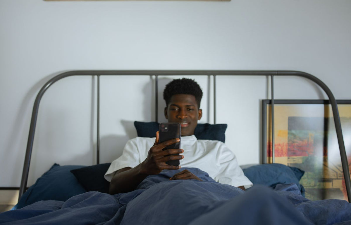 Young man using smartphone in bed, enjoying leisure time at home.