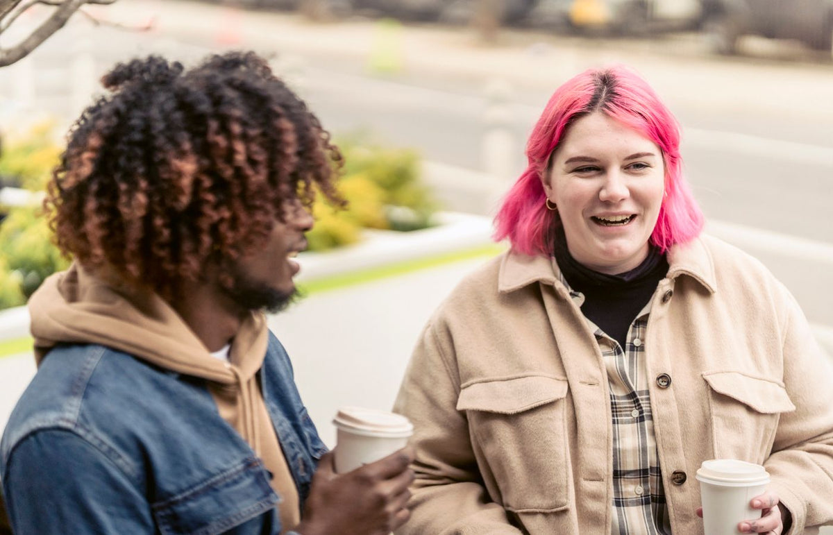 Two friends enjoying a coffee together outdoors, sharing a joyful conversation.
