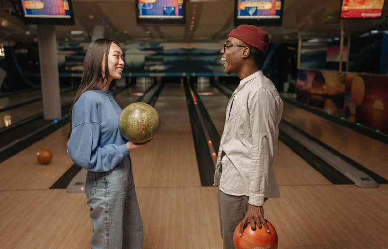 Friends enjoying a lively conversation while holding bowling balls at an indoor bowling alley.