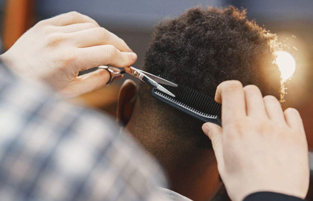 Close-up of a professional barber trimming an afro hairstyle with scissors and comb.
