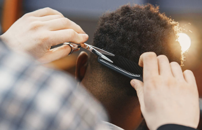 Close-up of a professional barber trimming an afro hairstyle with scissors and comb.